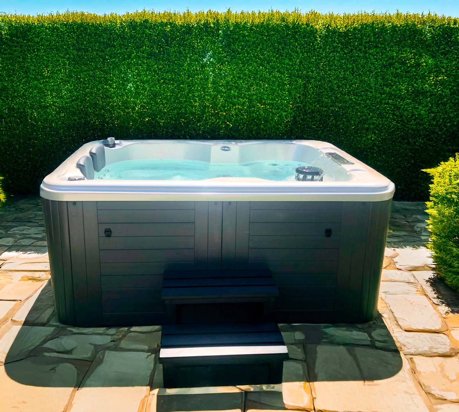 Le spa Caraïbes 4 places installé en extérieur sur une terrasse en pierre, offrant un cadre relaxant.